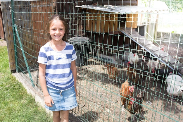 Girl child in the summer with a chicken coop in the garden