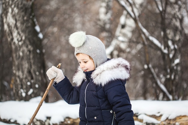 Girl child walking in the winter forest in a blue jacket and gray hat