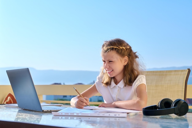 Girl child with headphones is studying using a laptop