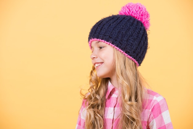 Girl child with long blond hair in hat plaid shirt smile on orange background beauty look hairstyle fashion style trend happy childhood concept copy space