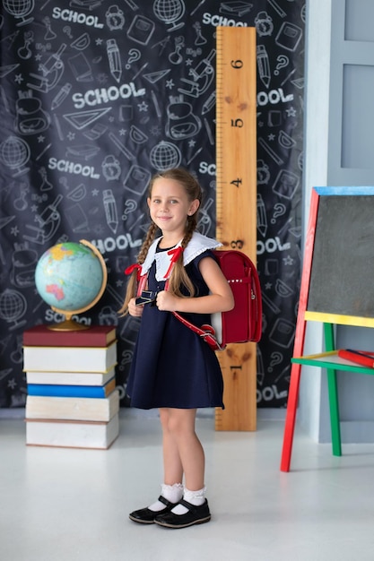 Girl Child with red backpack studies in classroom against background of black board in school