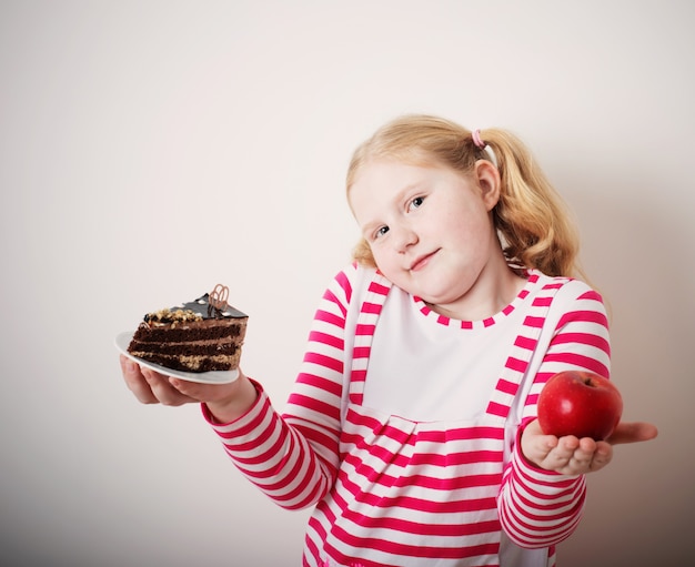 Girl choose from sweet cake and red apple