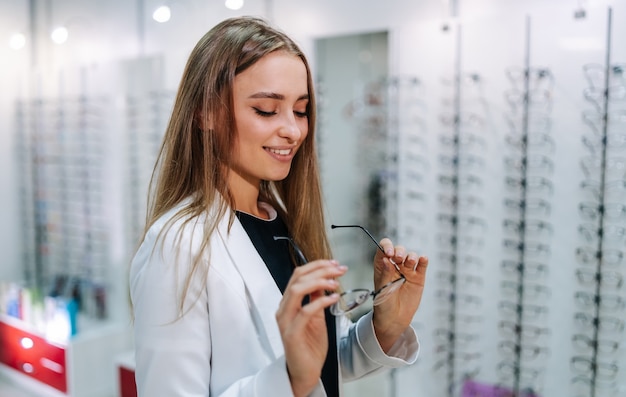 眼鏡店で矯正眼鏡を選ぶ女の子。ぼやけた背景に眼鏡をかけて生。 oftalmologyショップの長い髪のかわいいクライアント。