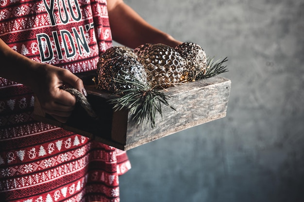 La ragazza in un vestito di natale tiene le palle in una scatola di legno, vacanza, comfort