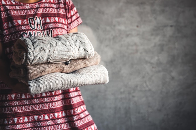 A girl in a Christmas dress holds a stack of sweaters. Warmth, comfort