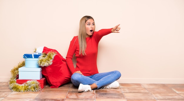 Ragazza nelle feste di natale che si siedono sul pavimento che indica via