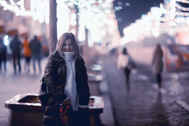 Ragazza luci natalizie sera città decorata, una giovane modella sullo sfondo di decorazioni urbane e ghirlande, luci notturne della città