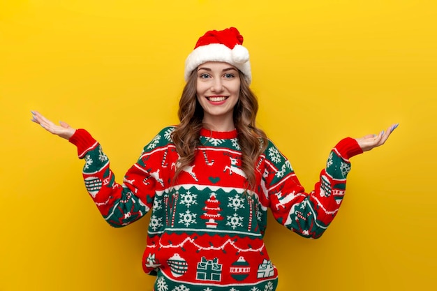 Girl in christmas sweater and santa claus hat spreads her arms to the sides on yellow background