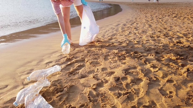 Girl cleaning plastic on the beach volunteers collect trash in\
a trash bag plastic pollution of oceans sustainability concept\
voluntary cleaning of nature from plastic and cleaning planet