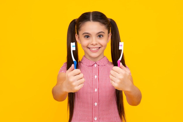 Girl cleans her teeth with a brush Portrait beautiful teen holding toothbrush brushing teeth isolated on yellow background Dental health concept Happy teenager positive and smiling emotions