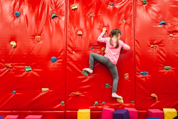 Girl climbing on a wall in childrens attraction playground. Entertainment center. Happy childhood