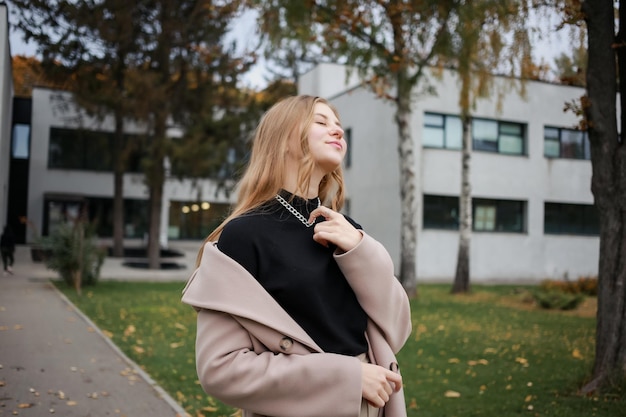 A girl in a coat and a black sweater straightens the silver chain around her neck