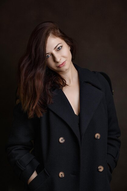 Girl in a coat on a dark background, brunette close-up