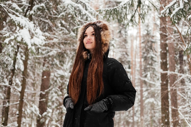 Girl in coat and gloves standing in winter fosert young woman with long brown hair in park outdoors