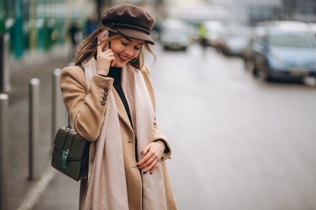 Ragazza in cappotto e cappello strillone parlando su un telefono