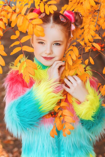 A girl in colored clothes among autumn yellow leaves of rowan