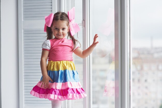 Girl in the colorful dress touching the window glass