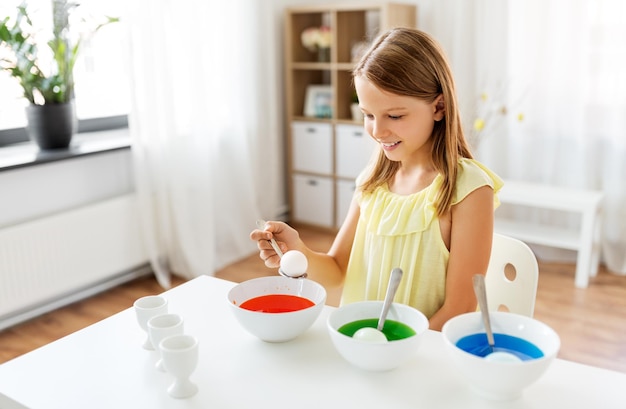 girl coloring easter eggs by liquid dye at home