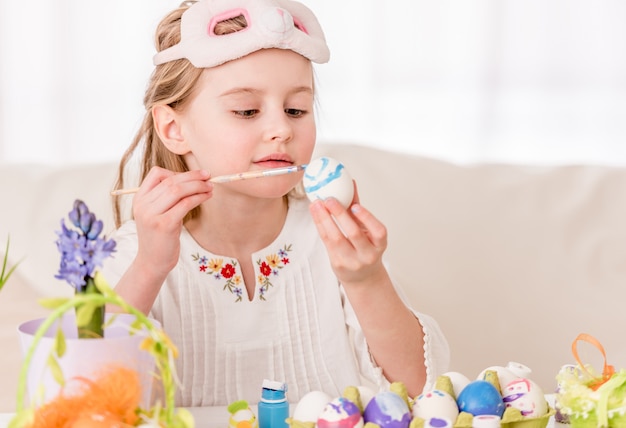 Girl coloring eggs in mask