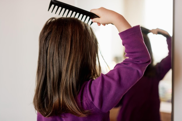 Girl combing her hair with comb in front of mirror