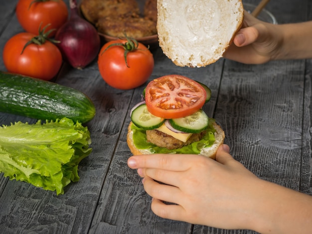 The girl completes the preparation of a delicious homemade hamburger with meat and vegetables