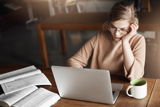 Ragazza che si concentra sul lavoro, corregge saggi, si appoggia la testa mentre è seduto al bar, lavora con il laptop, beve il tè per concentrarsi e prende appunti, controlla i dati nel conto aziendale