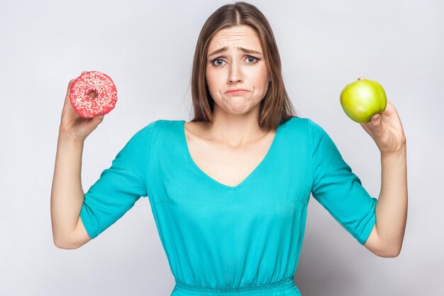 Photo girl confussed and trying to make choice between apple and donut