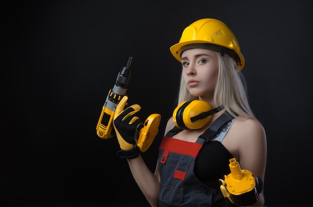 The girl in construction clothes and protective equipment posing with a screwdriver