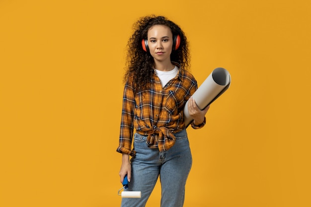 A girl in construction headphones and with a roller and paper in her hands