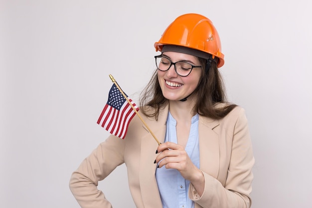 A girl in a construction helmet and an American flag stands happy on a white background