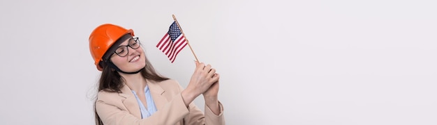 A girl in a construction helmet and an American flag stands happy on a white background