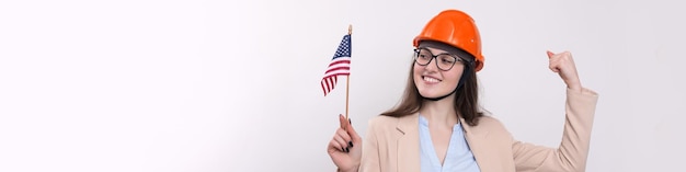 A girl in a construction helmet and an American flag stands happy on a white background