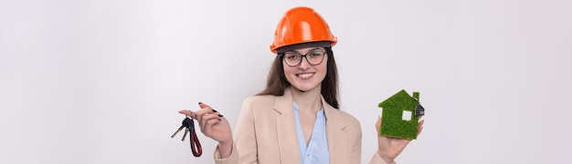 A girl in a construction helmet holds a green house The concept of ecological clean housing