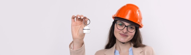 A girl in a construction helmet holds a house Realtor on a white background