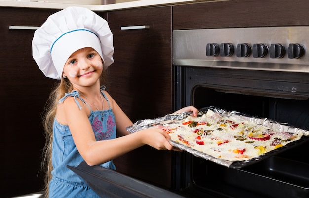 girl in cook cap near oven with pizza