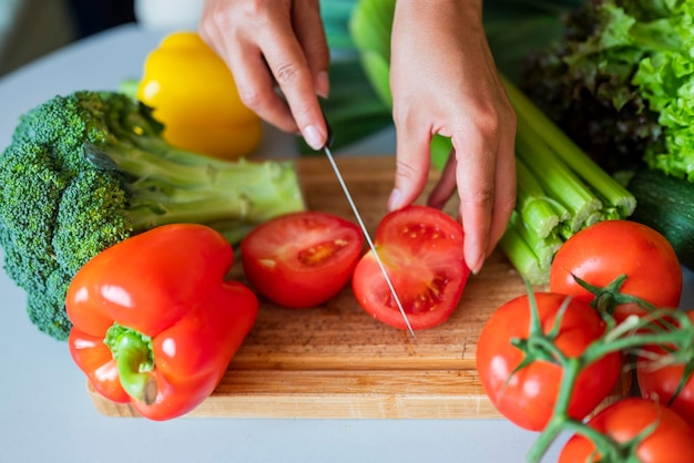 Ragazza cuoca in cucina taglia un pomodoro con verdure con un coltello