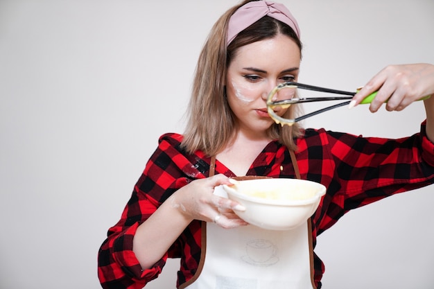 料理をしている女の子、エプロンを着た女の子、小麦粉で汚れた面白い女の子、生地をむち打ちます