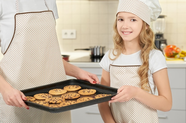 Girl in cooking hat and apron keeping tray with cookies