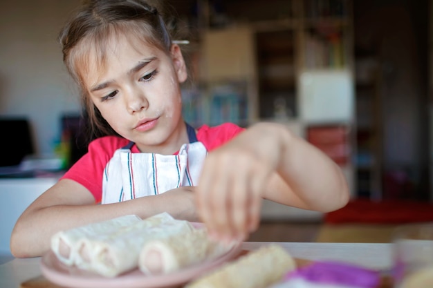 Girl cooking sausage rolled in phyllo pastry for breakfast little chef enjoys tasty snack