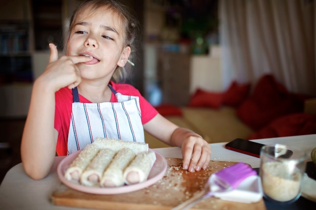 Girl cooking sausage rolled in phyllo pastry for breakfast little chef enjoys tasty snack