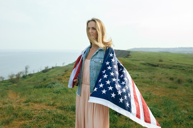 A girl in a coral dress and a denim jacket holds the flag of the united states in her hands. July 4th Independence Day.