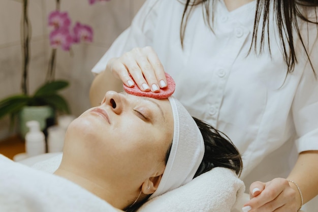 女子美容師がスクラブスポンジで患者の顔を掃除する
