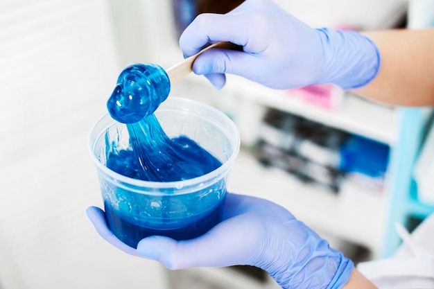 A girl cosmetologist holds blue sugar paste for hair removal on a spatula in a beauty salon Spatula