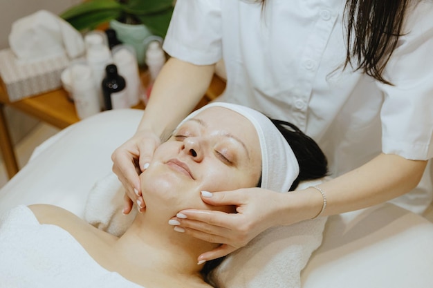 a girl cosmetologist massages the patient s face with her fingers