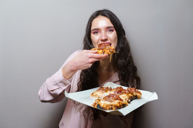 Girl courier eating pinsa pizza romana gourmet italian cuisine. Holding scrocchiarella traditional dish. Pinsa with meat, arugula, olives, cheese.