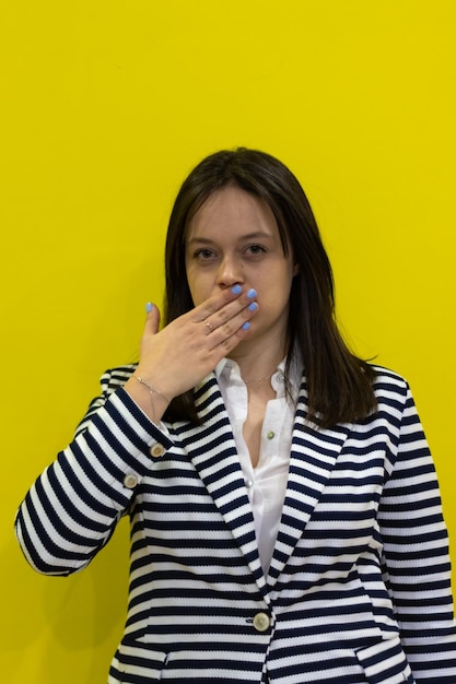 Girl covering her mouth on isolated yellow background Woman covering her mouth on a yellow background