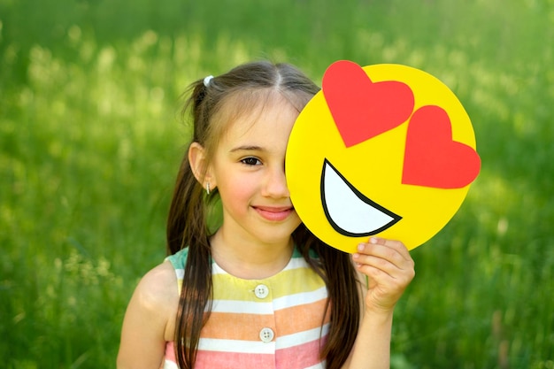 La ragazza copre il viso con un'emoticon sorridente amorevole con i cuori