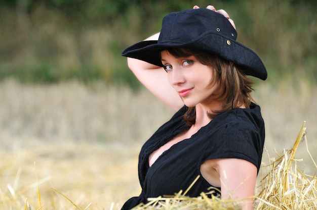 Girl in cowboy hat sits on haystack