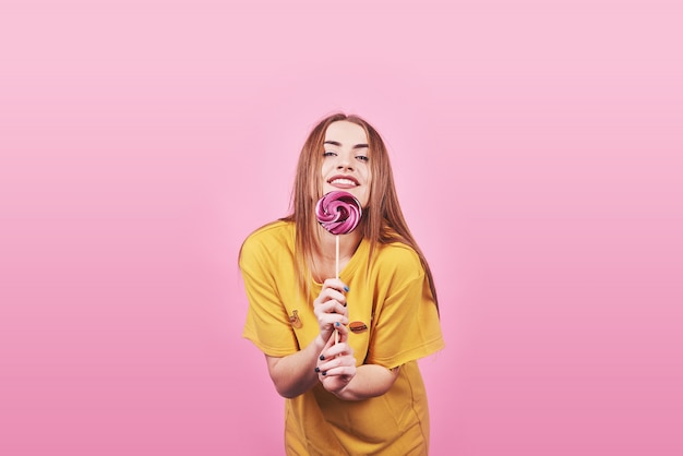 Girl cute funny portrait holding lollipop smiling on pink