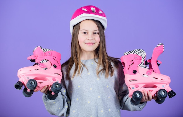 女の子かわいい十代は紫色の背景にヘルメットとローラースケートを着用ローラースケート十代の趣味うれしそうな十代は乗るスポーティーな十代の少女ローラースケートの準備ができてアクティブなレジャーとライフスタイル